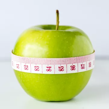 a green apple with a measuring tape wrapped around it, shown in centimeters showing numbers 81-88