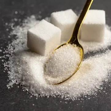 three cubes of sugar in a pile of granulated sugar with a gold tea spoon
