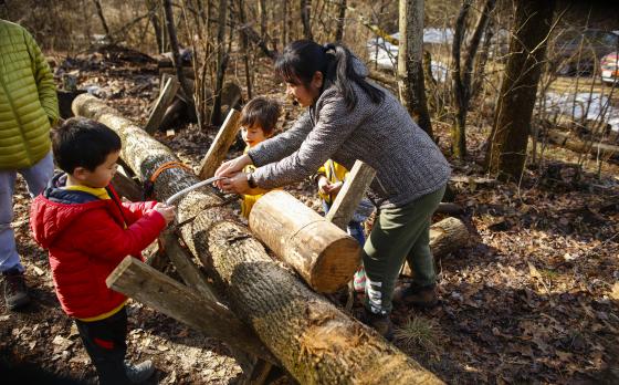 a mom and two kids participating in the Maple Syrup event at the Y at Watson Woods by sawing a log by hand