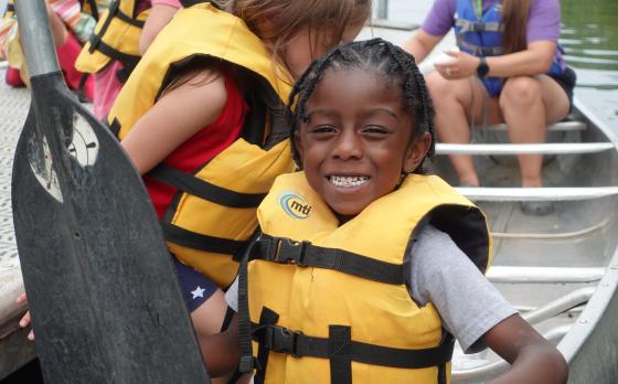a young boy smiling in a canoe wearing a life vest