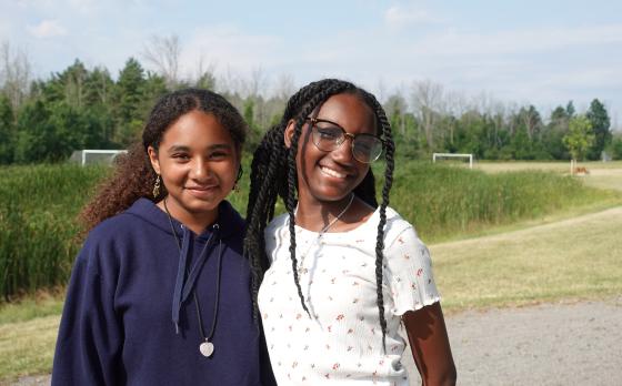 two girls standing in front of a field at YMCA Camp Northpoint smiling at the camera