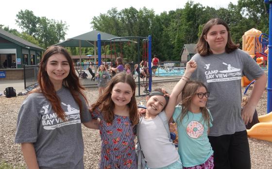 three kids and two counselors at a playground at YMCA Camp Bay View