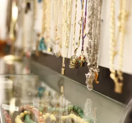 various necklaces hanging on a board with bracelets in a bowl below