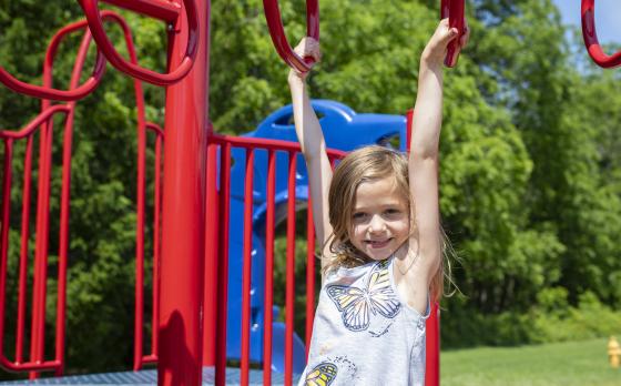 Blonde girl hanging from red monkey bars