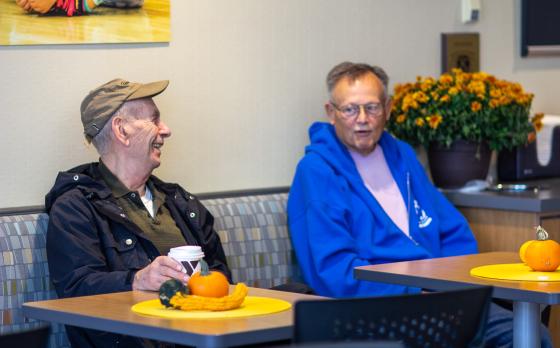 two older men sitting in the lobby at the Northwest Family YMCA smiling and talking over coffee