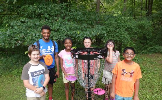 a group of campers with a counselor around a disc golf net