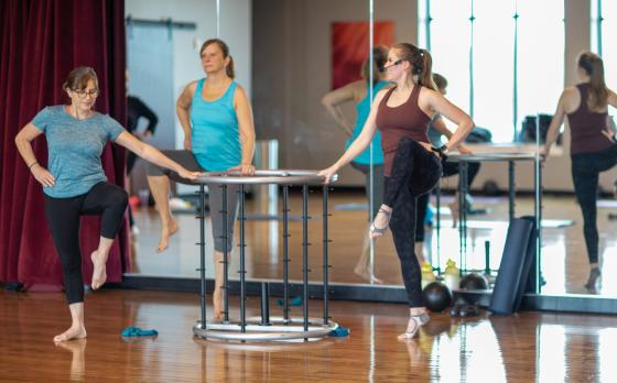 two women and an instructor share a piece of barre equipment during a class at the Schottland Family YMCA