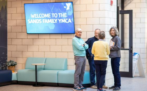 Four older adults standing outside of the rayburn family community room at the Sands Family YMCA
