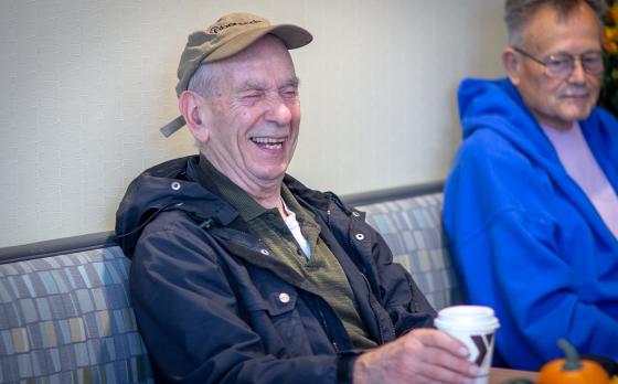 Older gentleman laughing in a lobby with a cup of coffee