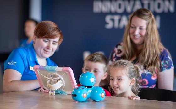 two children with a parent and ymca staff looking at an ipad that controls a robot in the West Herr Innovation Station
