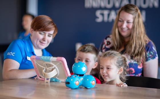 A mom, her son and daughter with a staff member playing with a robot
