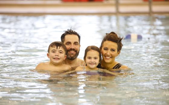 a mom and dad in the pool with their son and daughter smiling at the camera