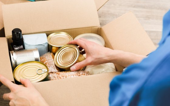 photo of person fill cardboard box with nonperishable foods and canned goods 