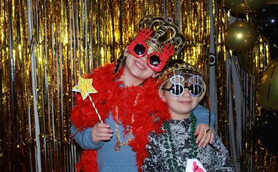 Two young kids in front of gold streamers smiling with novelty new years glasses