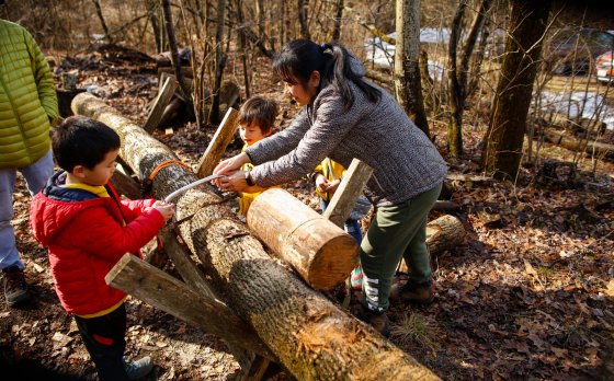 a mom and two kids participating in the Maple Syrup event at the Y at Watson Woods by sawing a log by hand