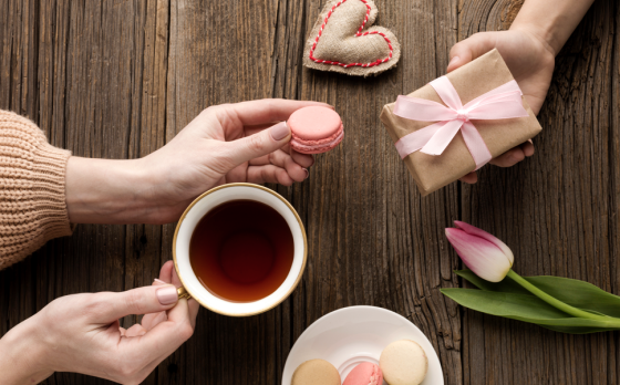 Treats and gifts being exchanged on a wooden table with tea, stuffed heart and tulip