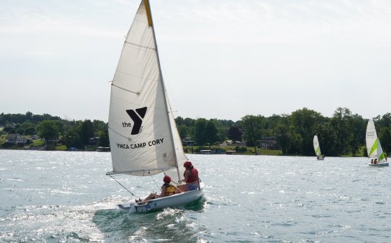two campers sailing on keuka lake on a sailboat that says "YMCA Camp Cory" with a Y logo on it