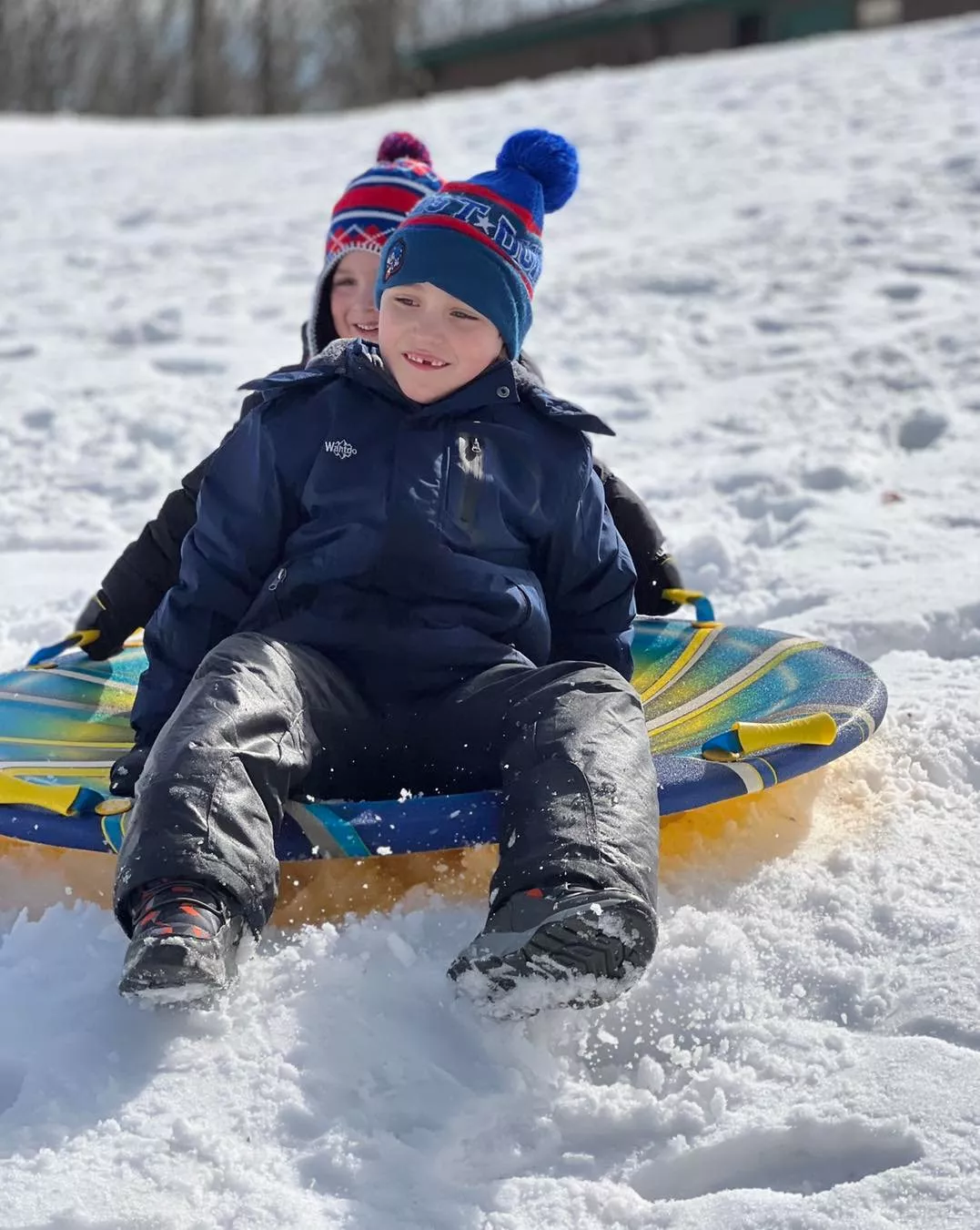 two kids sledding down a snowy hill