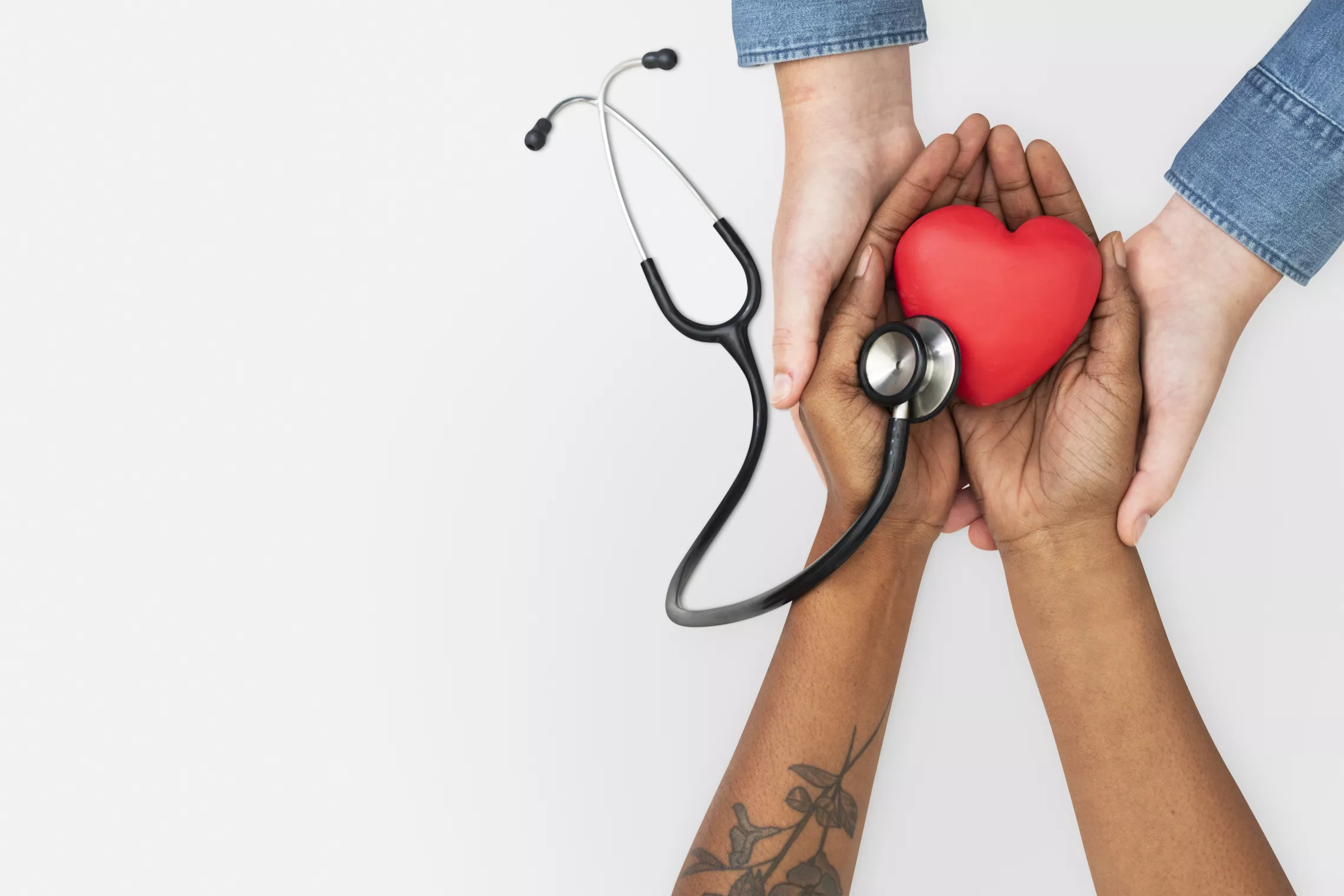 a pair of hands holding another pair of hands. The second pair of hands is holding a foam heart and a stethoscope