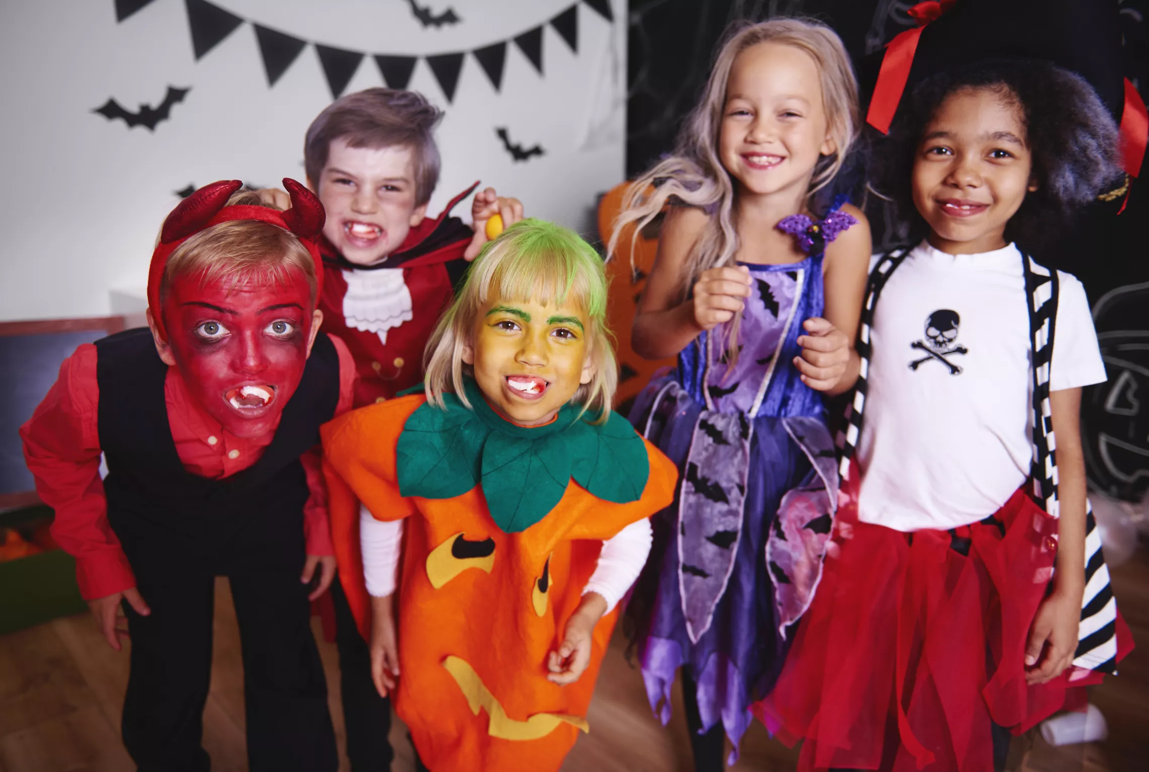 five children dressed up for halloween. the costumes are from left to right: devil, vampire, pumpkin, witch, pirate