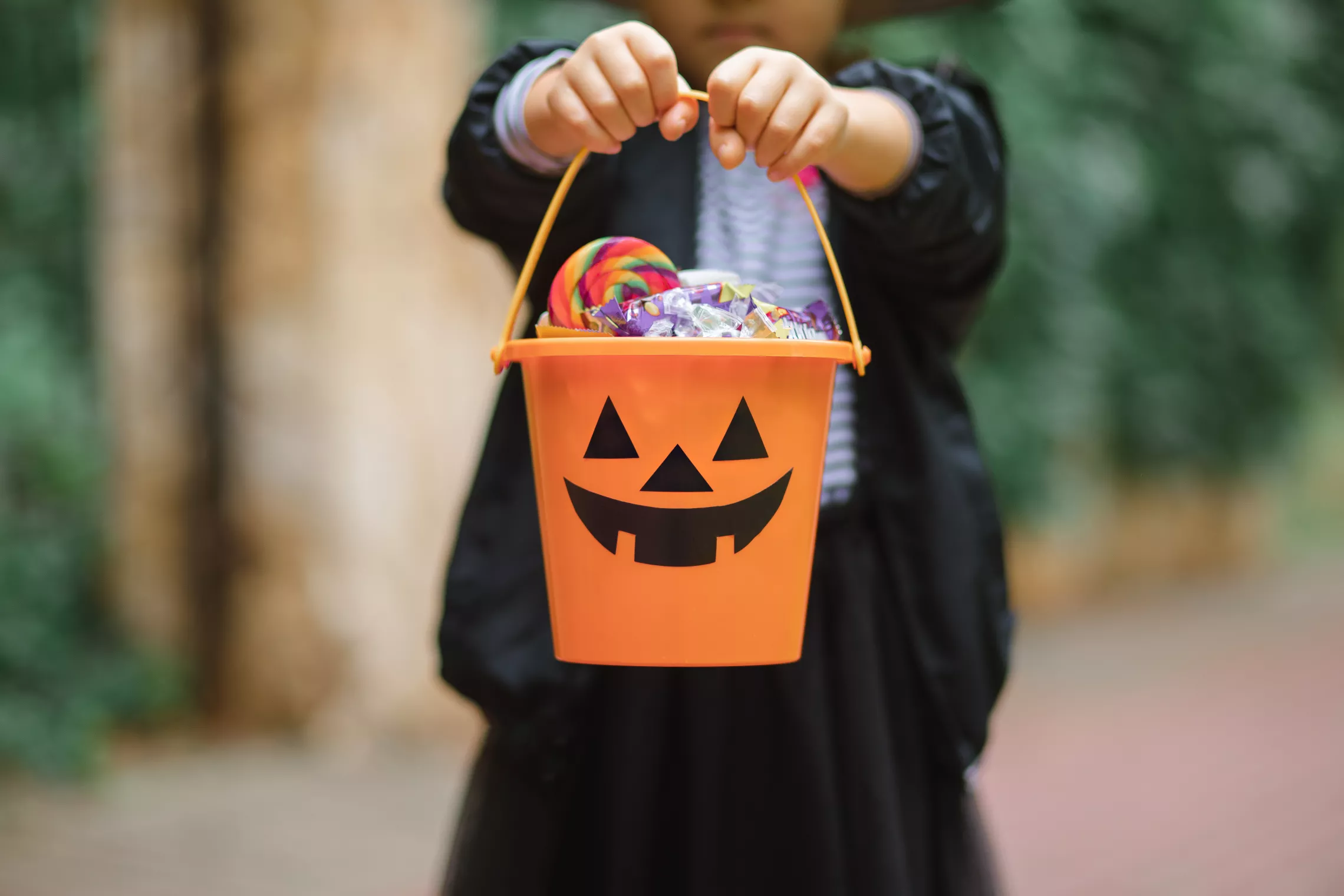 a child holding out a pail with a jack o lantern face on it that is filled with candy