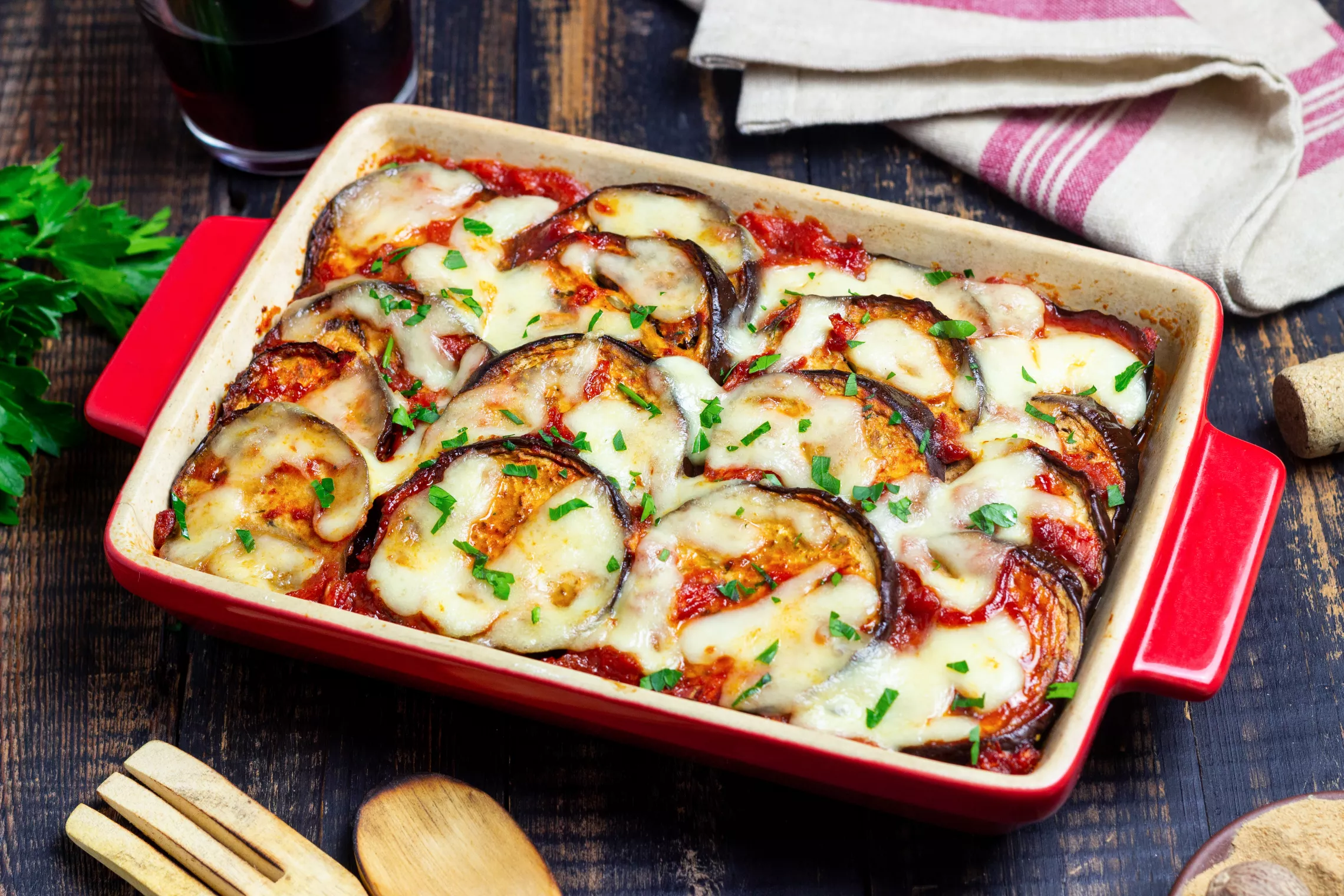 eggplant parmesan in a red casserole dish on a wood table