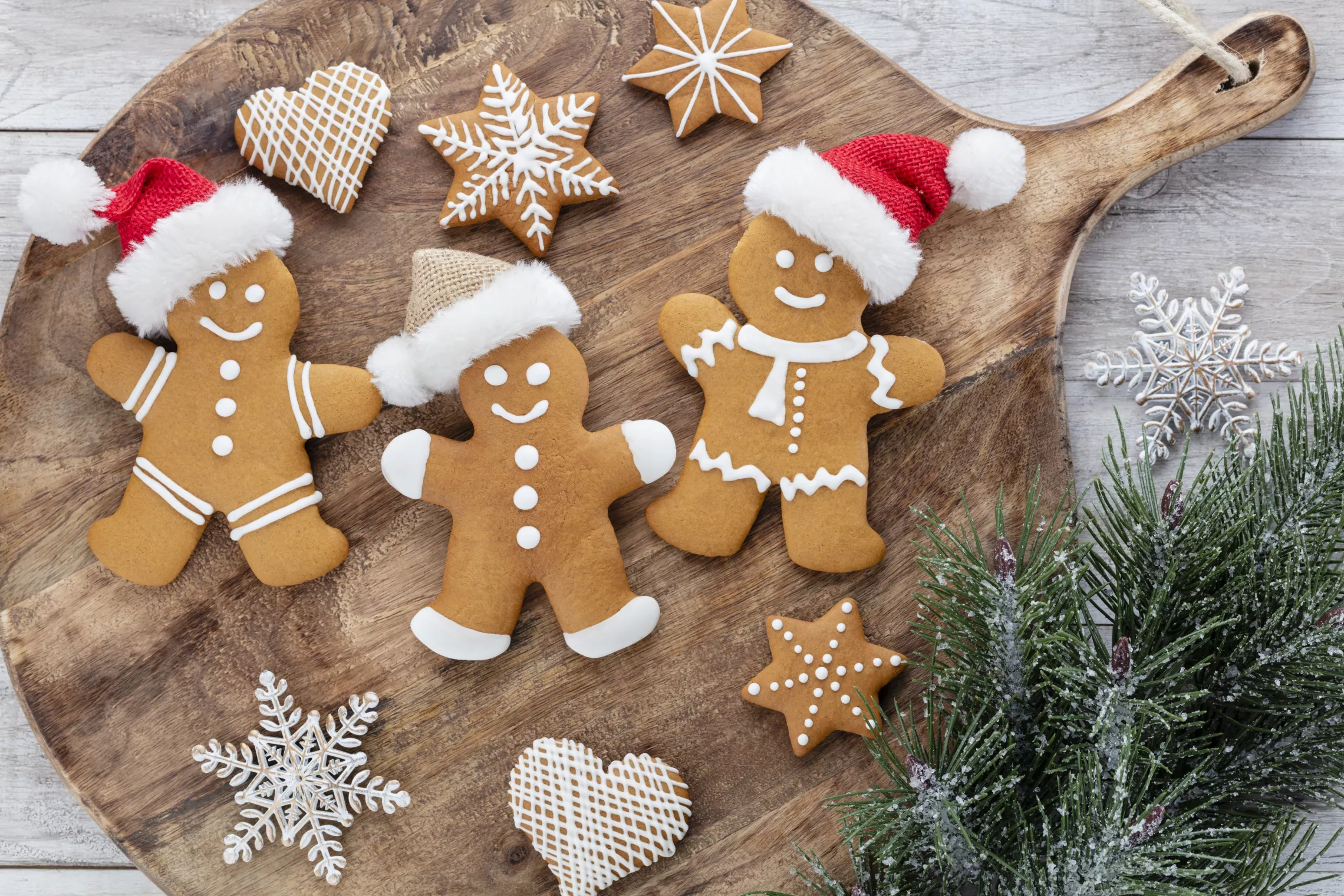 three gingerbread men, with other small gingerbread cookies on a wood serving platter