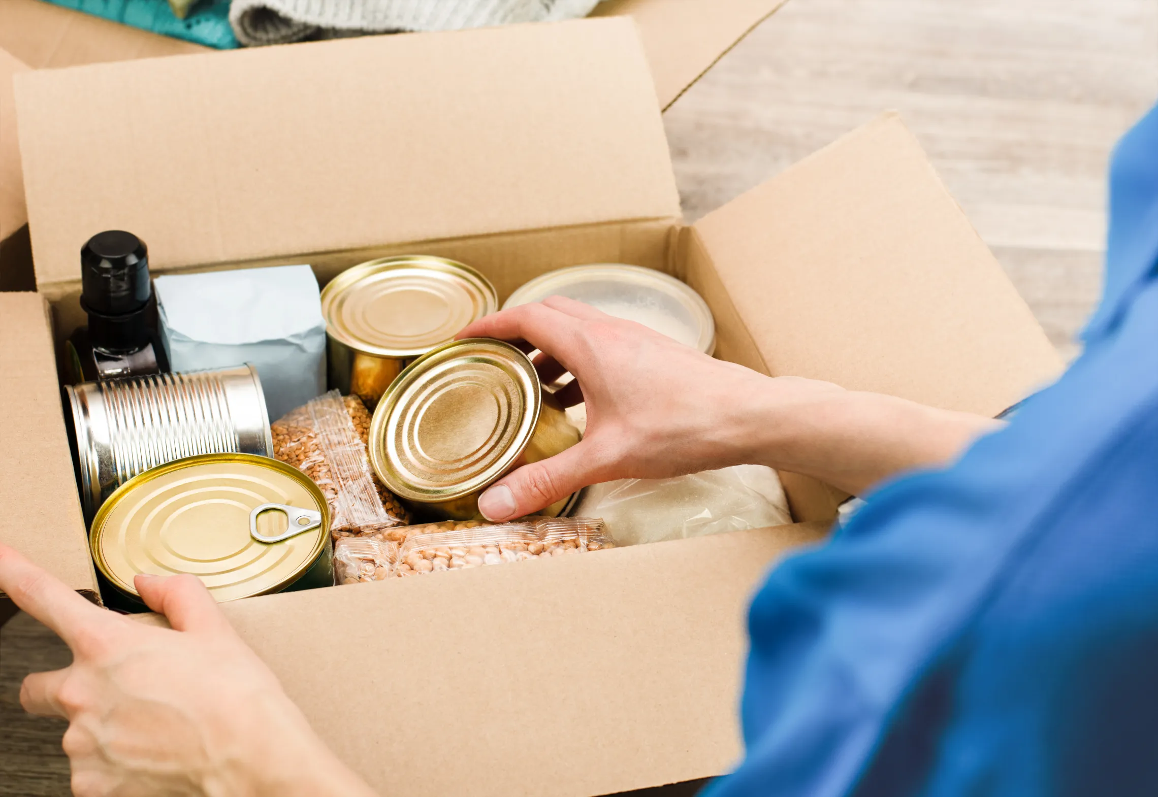 photo of person fill cardboard box with nonperishable foods and canned goods