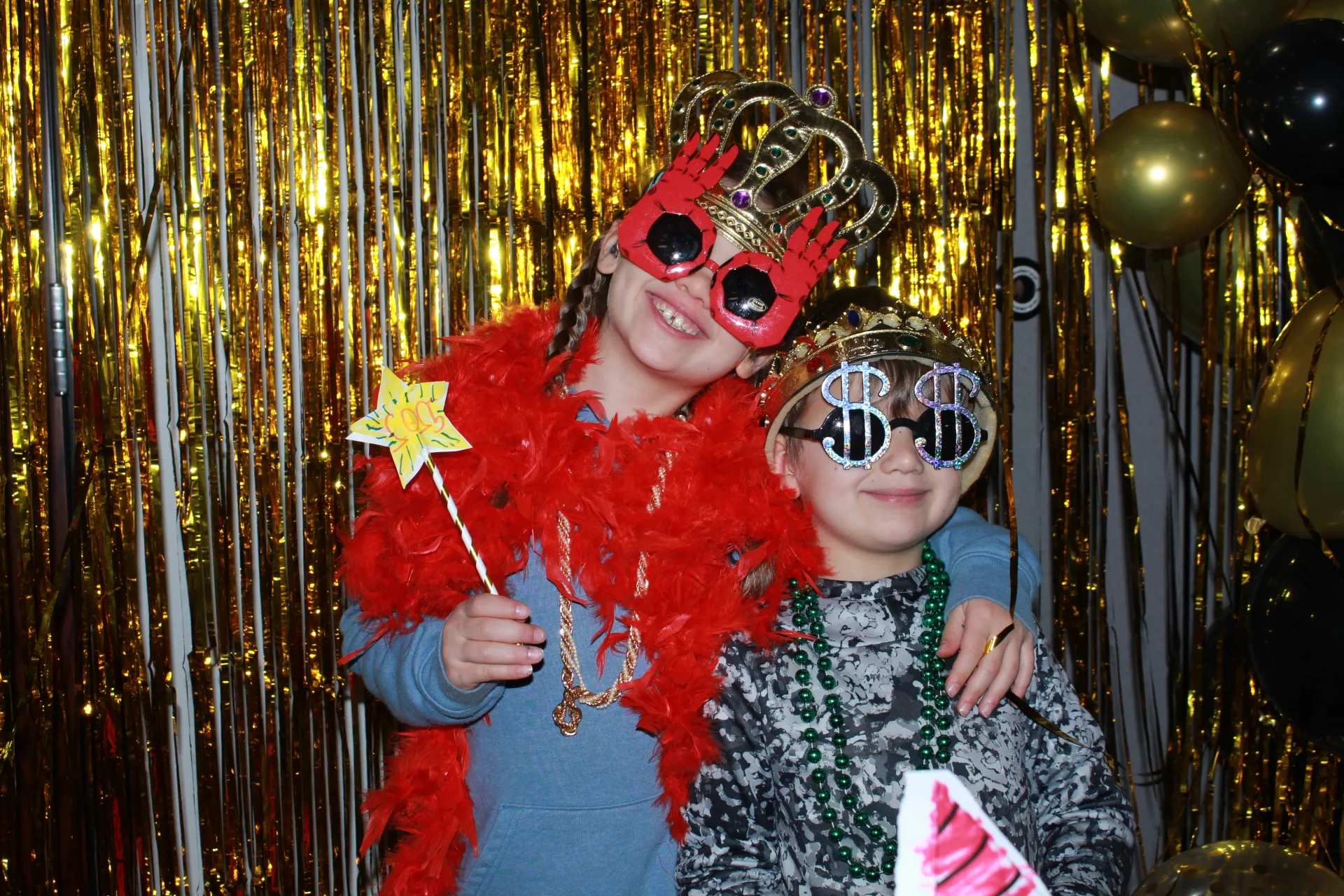 Two young kids in front of gold streamers smiling with novelty new years glasses