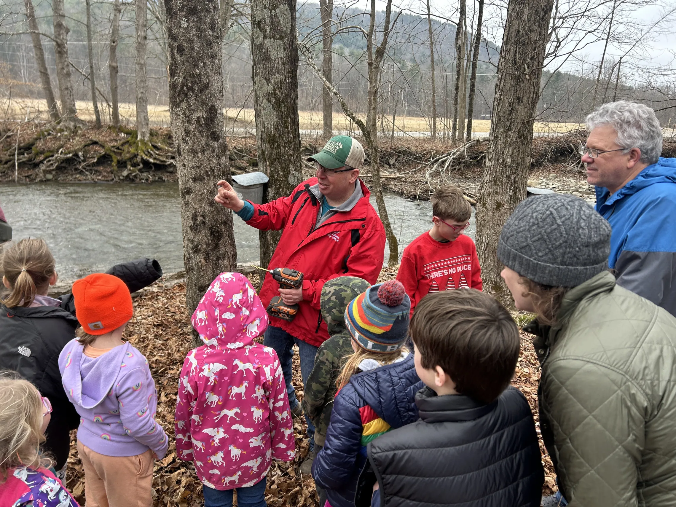 A group stand in the woods learning about tapping a maple tree.