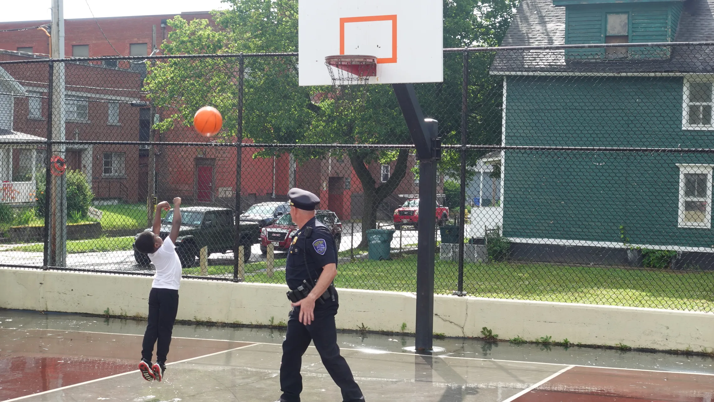 a police officer and a child playing basketball together on a outdoor basketball court