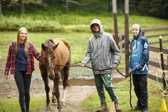 One counselor and two campers walking with brown horse