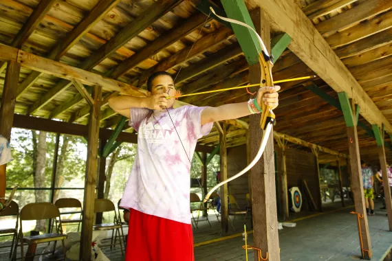 a camper at camp gorham with a bow and arrow at the archery range