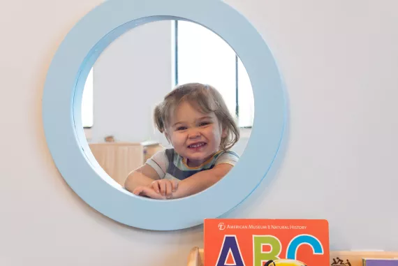a young girl looking through a small circle window in the Skalny Child Care Center