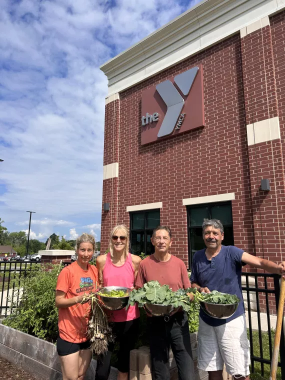 four members stand outside the garden showcasing a harvest of fresh produce