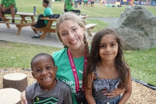 A summer camp counselor at Camp Bay View sits with two campers 