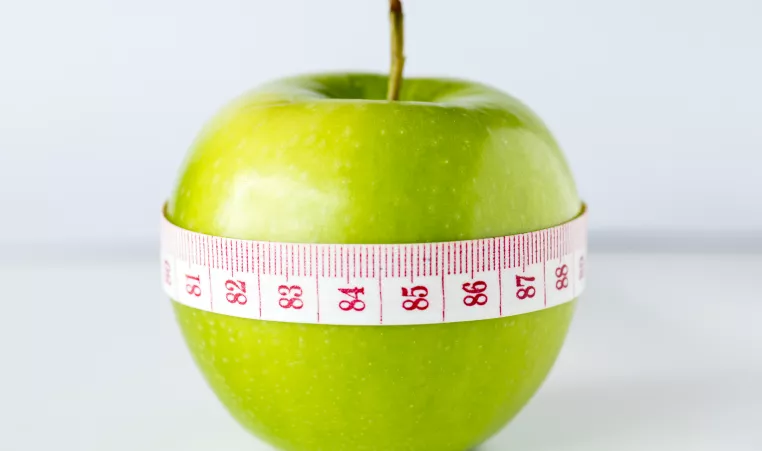 a green apple with a measuring tape wrapped around it, shown in centimeters showing numbers 81-88