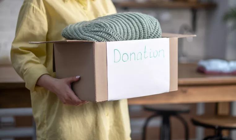 a woman holding a cardboard box labeled donation with a blanket sticking out from the box