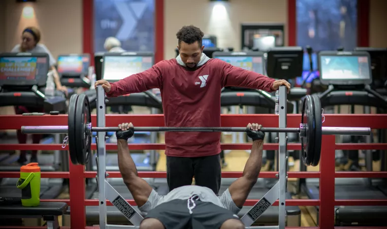 a ymca staff member spotting a member while he bench presses in the maplewood family ymca wellness center