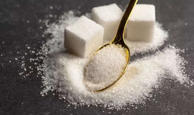 three cubes of sugar in a pile of granulated sugar with a gold tea spoon