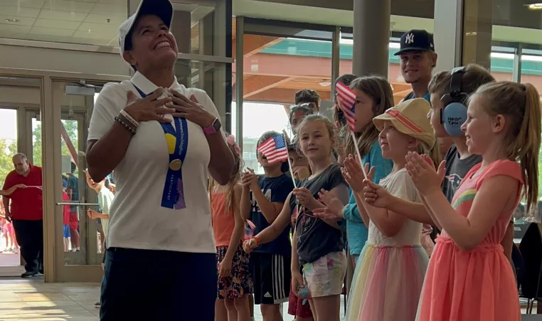 a group of young children clapping in the eastside ymca lobby as staff member amanda vito returns from participating in the special olympics in germany.