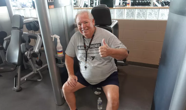 an older man sitting on a strength machine smiling and giving a thumbs up