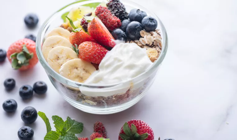 a smoothie bowl with bananas, strawberries, blueberries and granola in a glass bowl on a marble table