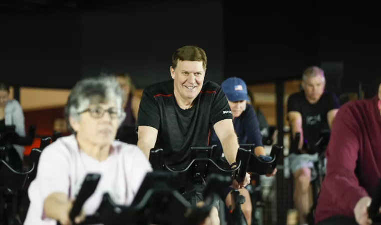 Man smiles while cycling in a YMCA group exercise class