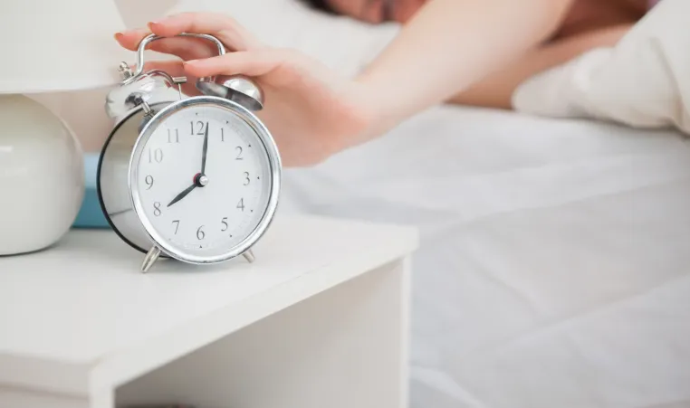 person turning off their alarm clock in bed