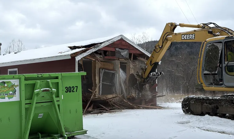 excavator being operated by BOCES student removing the outside wall of a cabin on property at The Y at Watson Woods