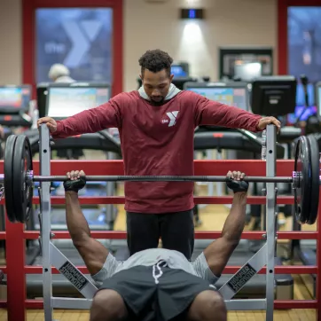 a ymca staff member spotting a member while he bench presses in the maplewood family ymca wellness center