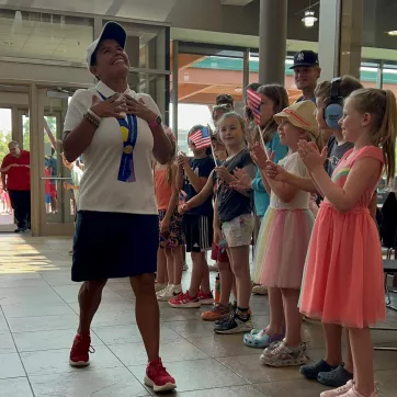 a group of young children clapping in the eastside ymca lobby as staff member amanda vito returns from participating in the special olympics in germany.