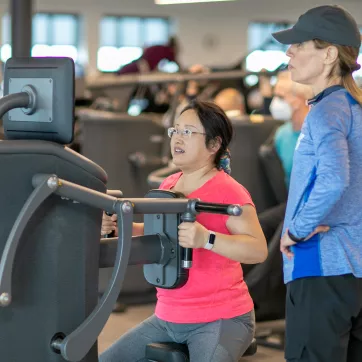 ymca member works out on egym equipment while staff helps give tips