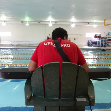ymca lifeguard sits at stand while on duty keeping water safe